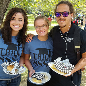 three students at fall fest smiling, two students are wearing TRIO shirts